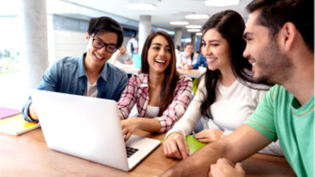 Smiling students around a laptop.